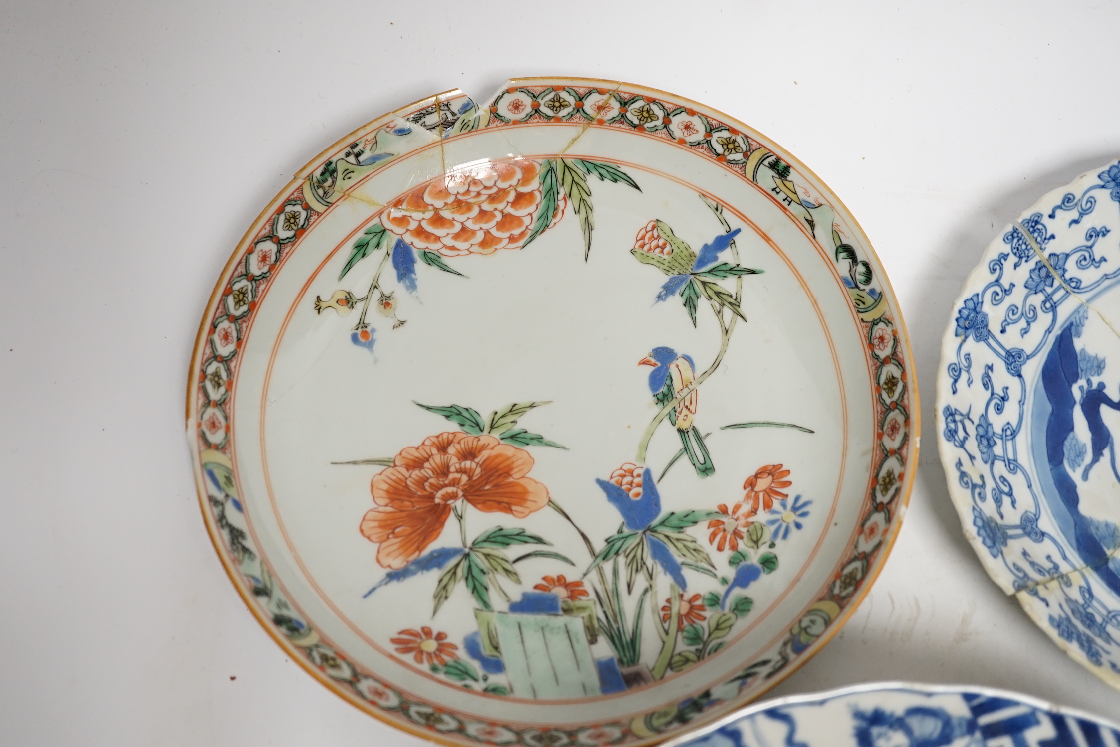 A Chinese blue and white ‘warriors’ bowl, Kangxi mark and period, a similar ‘hunting’ saucer dish, and a famille verte saucer dish, all Kangxi period (3), largest 27cm in diameter